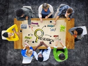 People sitting at a table around a chart that reads RESEARCH